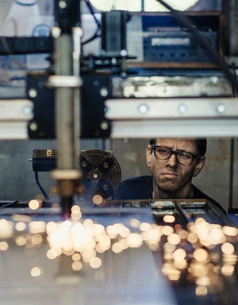 A manufacturing worker looking at a metal plate which is being welded