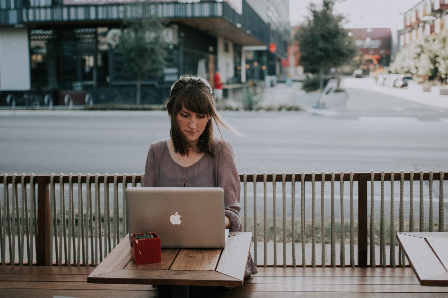 a woman who is working remotely on a macbook outside a coffeeshop